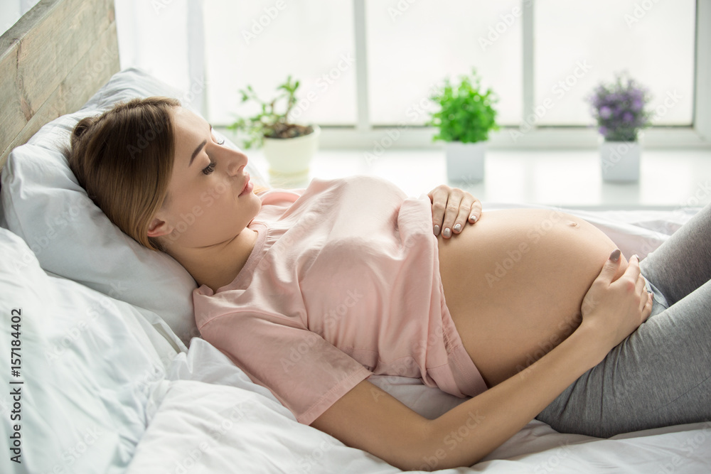 Young preganant woman expecting a baby relaxing on bed indoors Young preganant woman expecting a baby relaxing on bed indoors