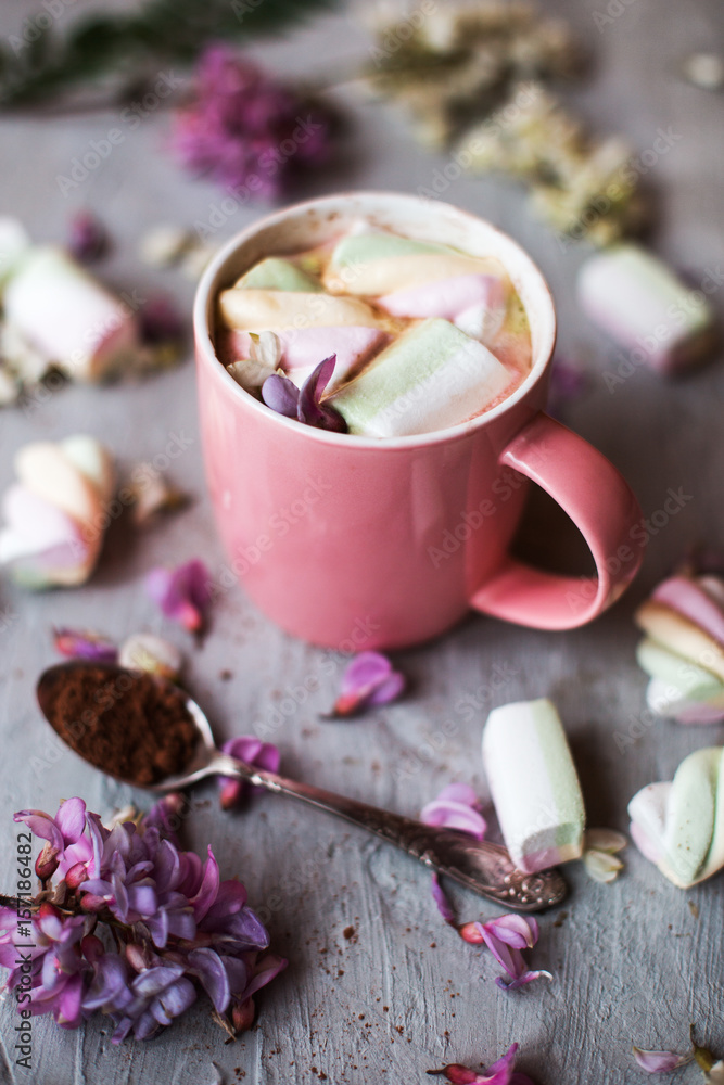 A large cup of cocoa and marshmallows on a neutral concrete background, decorated with flowers.