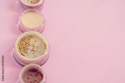 Woman mineral beauty makeup kit, loose powder, bronzer, concealer, highlighter on pink colored background. Flatlay