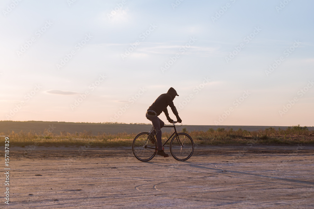 Fototapeta premium Alone rider on fixed gear road bike riding in the desert near river, hipster tourist bicycle rider pictures.