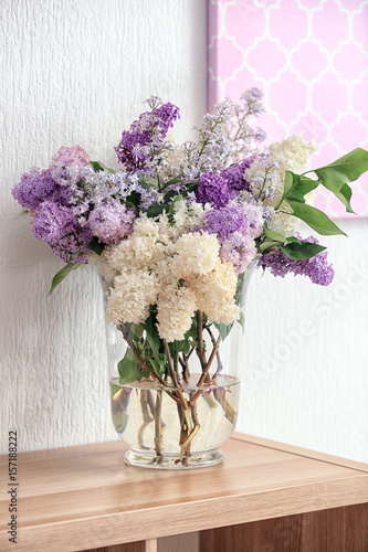 Glass vase with beautiful lilac flowers on wooden table