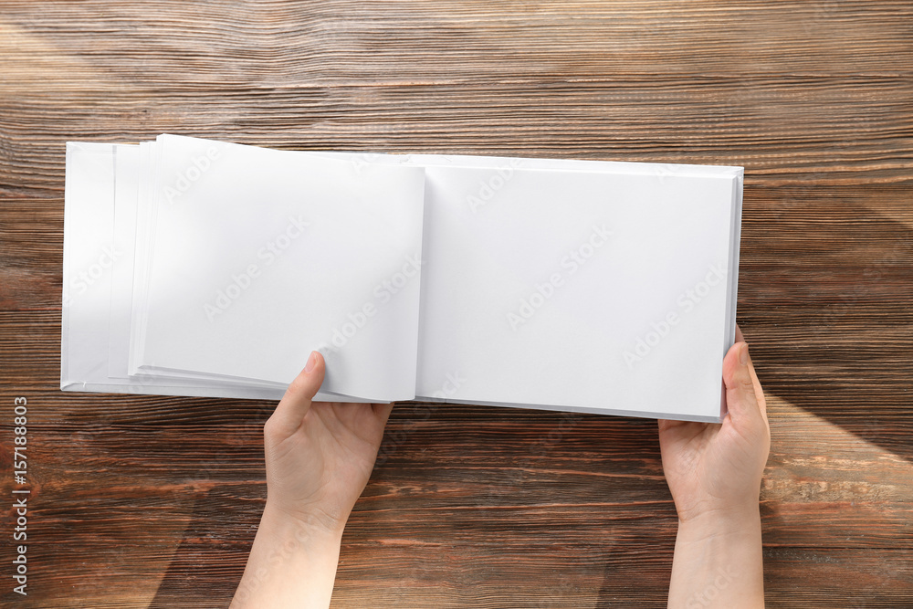Obraz premium Female hands holding opened book with blank pages on wooden background