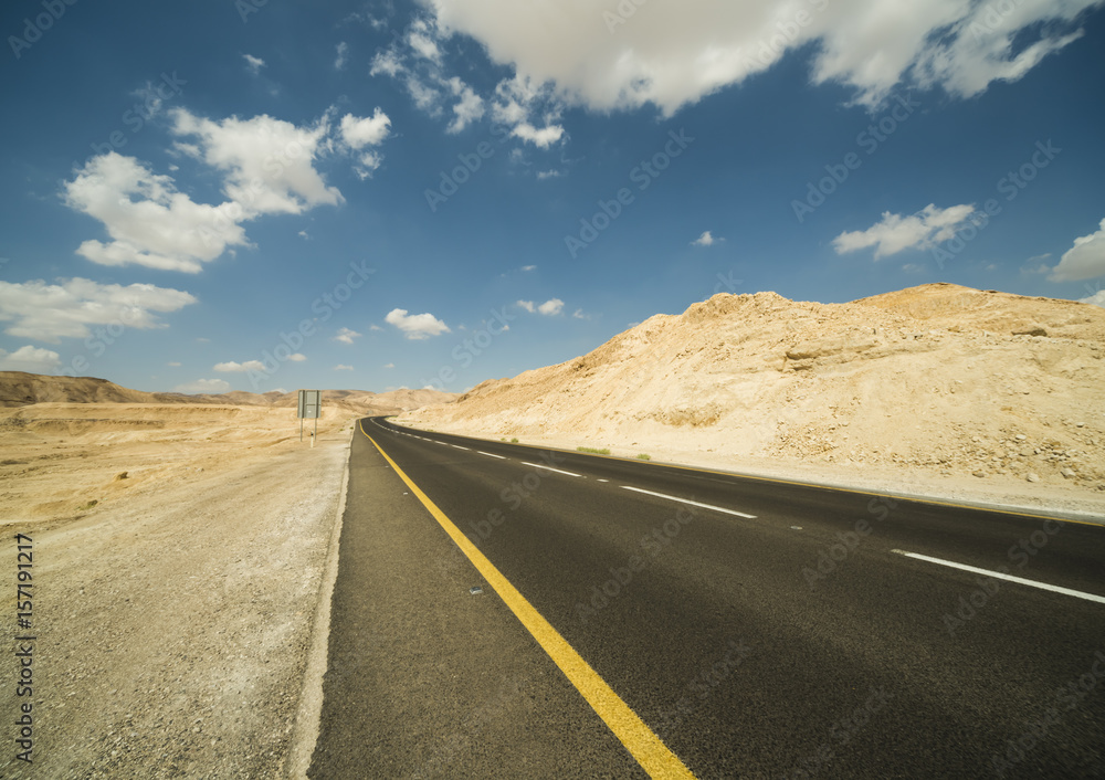 Asphalt road in the Judean desert on a background of blue sky with clouds