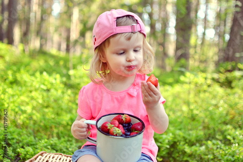 Little baby girl eating strawberries and blueberries in the park