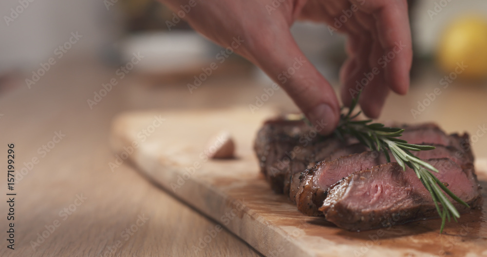 man decorating sliced medium rib eye steak with rosemary branch, wide photo