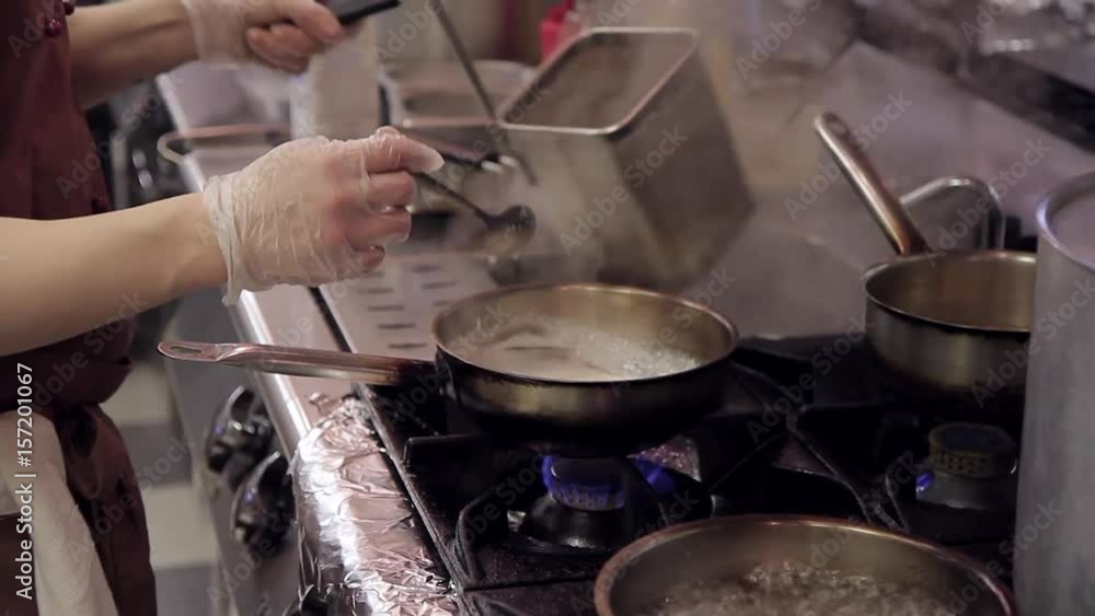 Cook after discarding pasta in a square sieve fry them in a pan. A woman in transparent gloves is standing by a burning gas stove, on which an Italian pasta is prepared. She quickly rinses the Cook after discarding pasta in a square sieve fry them in a pan. A woman in transparent gloves is standing by a burning gas stove, on which an Italian pasta is prepared. She quickly rinses the