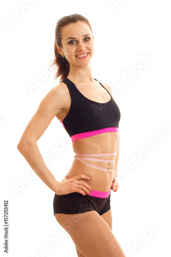 Slim athletic girl with the measuring tape at the waist keeps his hand on the side and smiling