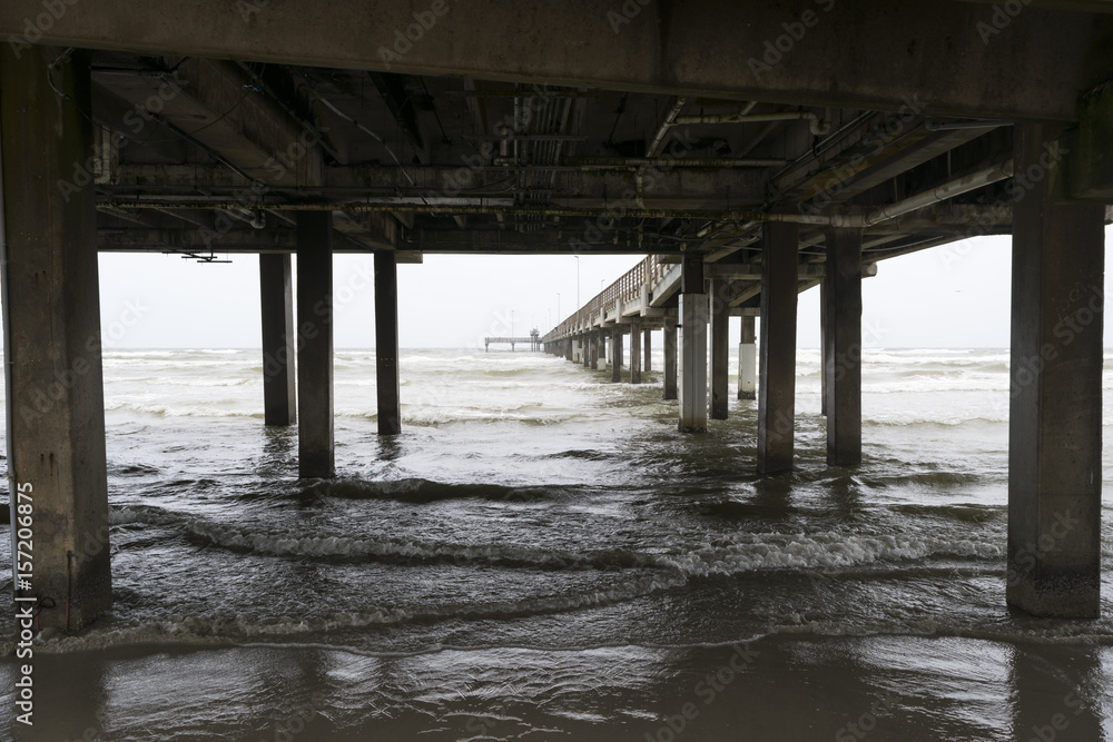 Ocean waves rolling onto the beach under a long pier