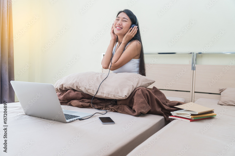 Obraz premium Beautiful asian woman wearing headset with labtop listening music on bed.