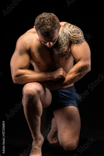 Shirtless muscular man bowing down, kneeling and looking down