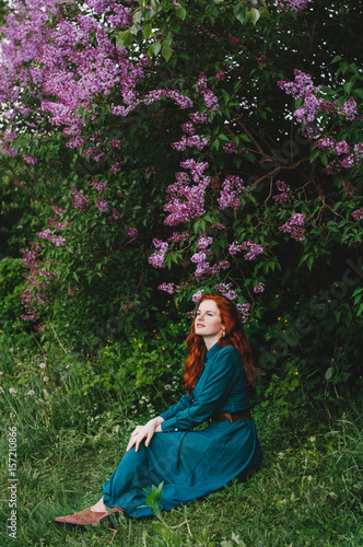 The red-haired girl is standing near the lilac bush