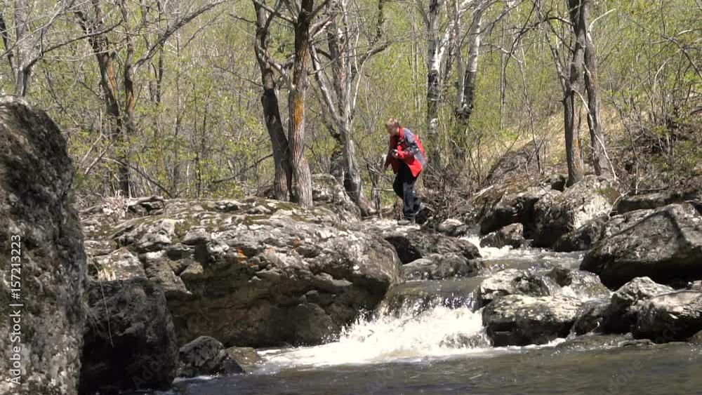 Young Man Blond Slow Motion Jumps a Forest Stream Over the Rocks. Early Spring is a Sunny Day, a Big Stream of Water. Young Man Blond Slow Motion Jumps a Forest Stream Over the Rocks. Early Spring is a Sunny Day, a Big Stream of Water.