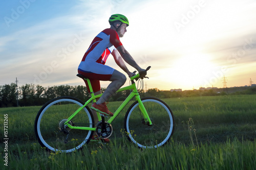 the cyclist on the field in the rays of the setting sun.