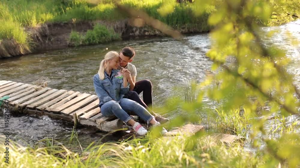 Lovers man and woman sitting on a wooden footbridge. Happy couple sitting on a makeshift wooden bridge over a shallow river Lovers man and woman sitting on a wooden footbridge. Happy couple sitting on a makeshift wooden bridge over a shallow river