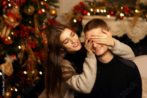 Cute lovers staying at home and enjoying tome together. Joyful girl close her husband or boyfriend eyes with her arms.