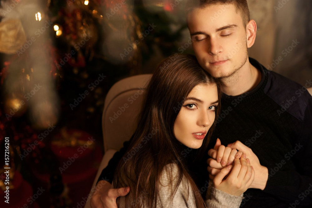 Closeup portrait of young romantic caucasioan couple sitting and higging in christmas decorated interior. Cute lovers staying at home and enjoying tome together