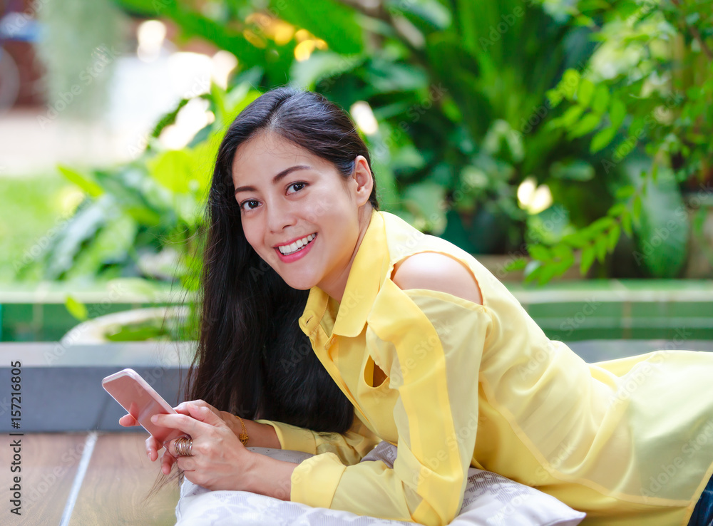 Smiling asian woman using smart phone looking at camera. Outdoors. Smiling asian woman using smart phone looking at camera. Outdoors.