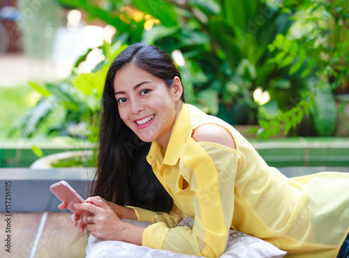 Smiling asian woman using smart phone looking at camera. Outdoors.