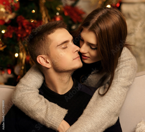 Young romantic cute couple staing at home and enjoying time together. Lovers hugging in cristmas decorated interior