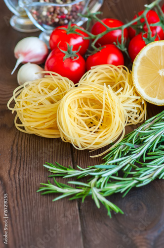 Raw ingredients for italian style dinner. Pasta, cherry tomatoes, garlic, rosemary on a wooden table. Close up and copy space.