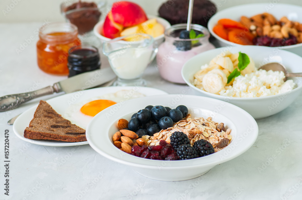 Healthy breakfast - granola with blackberry, dry cranberry, blueberry, almond, cottage cheese with banana, fried eggs with bread, yogurt, jams, nuts, sour cream on a white background. Healthy breakfast - granola with blackberry, dry cranberry, blueberry, almond, cottage cheese with banana, fried eggs with bread, yogurt, jams, nuts, sour cream on a white background.