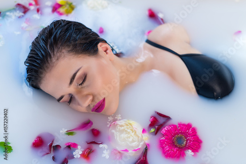 Closeup view of Woman in bath. Sexy brunette woman relaxing in hot milk bathtube with flowers. she is wearing black sexual lingerie. Spa satisfaction