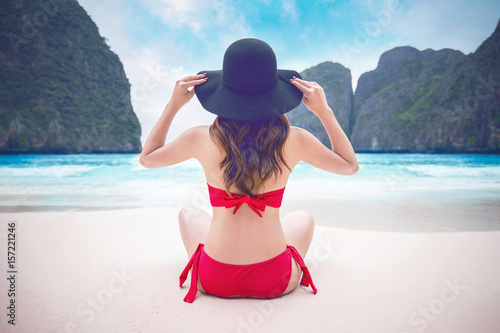 Young woman in red bikini sitting on the beach.