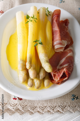 Healthy food: white asparagus with hollandaise sauce and ham close-up. vertical