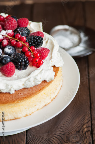 Close up of fluffy Japanese cotton cheesecake with wipped cream cheese frosting and garnished with forest berries served on a plate over wooden background. Rustic style