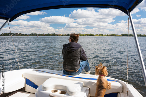 Man with his dog in motor boat on the river. Summer vacation yacht sailing, water sport. Yachtsman traveling by motorboat, unrecognizable person, sunny summer outdoor on blue cloudy sky background
