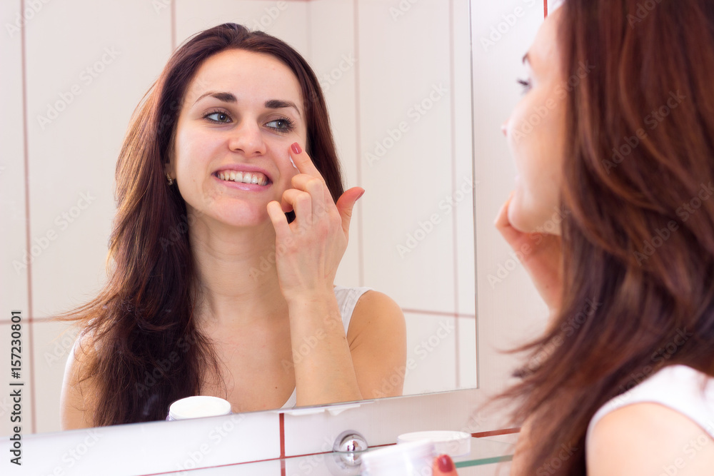 Young woman using face cream in bathroom Young woman using face cream in bathroom