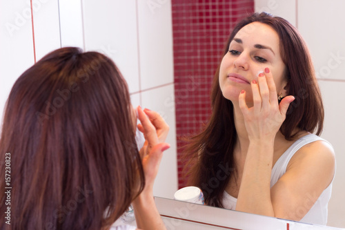 Young woman using face cream in bathroom
