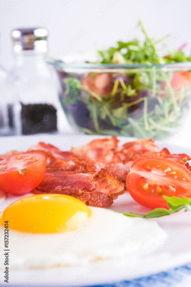 Breakfast with fried eggs and bacon with fresh salad and toast on the table.