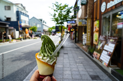 Enjoying milk ice cream soft serve cone with green tea flake powder on street footpath on sunny day