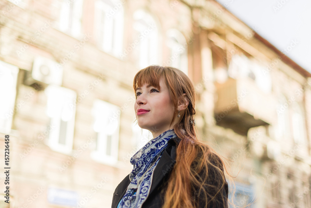 Beautiful red-haired young woman walking down the city street on a sunny day, examining the neighborhood. Beautiful red-haired young woman walking down the city street on a sunny day, examining the neighborhood.