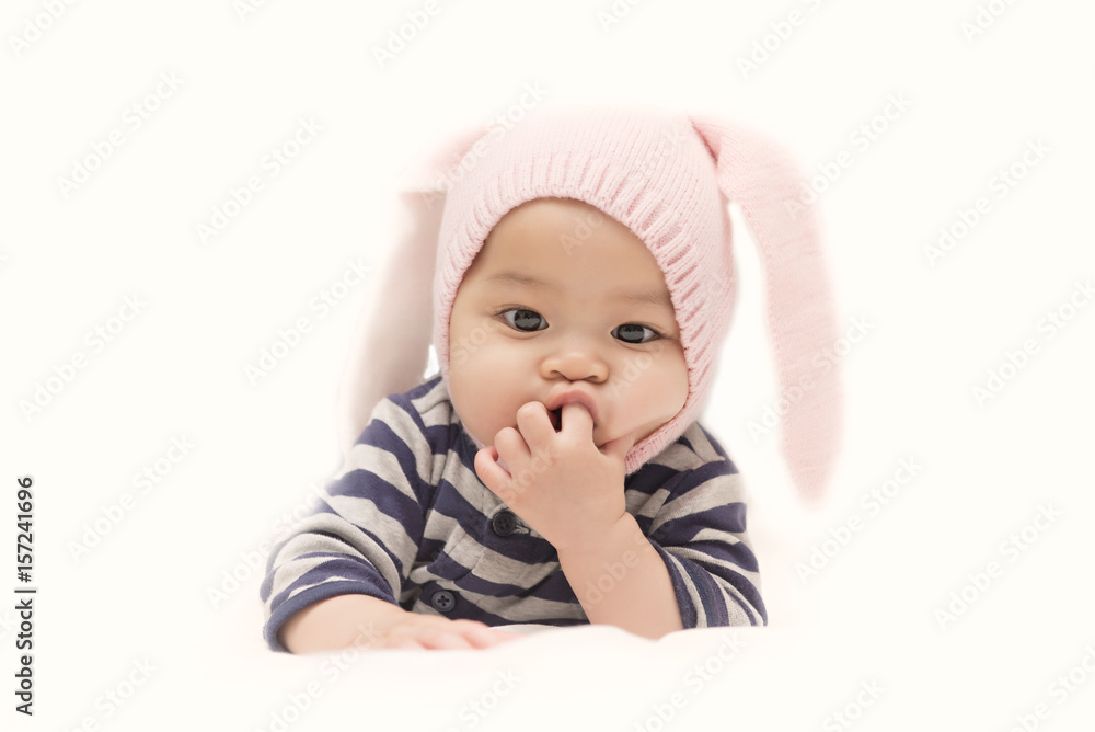 Charming Asian child. Little girl with rabbit hat lying on her stomach and sucks fingers. Charming Asian child. Little girl with rabbit hat lying on her stomach and sucks fingers.