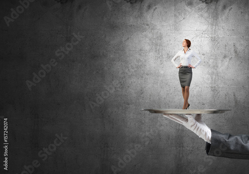 Confident elegant businesswoman presented on metal tray against concrete wall background