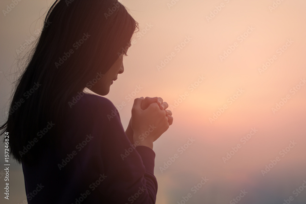 Christian woman praying worship at sunset. Hands folded in prayer