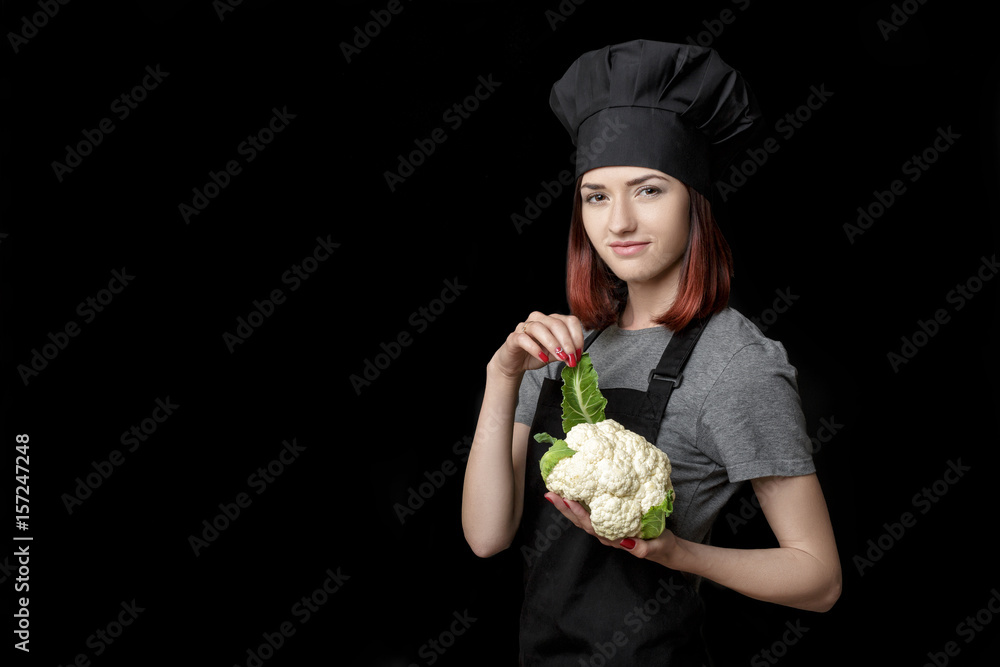 Young attractive woman chef in black uniform holds Fresh cauliflower on black background Young attractive woman chef in black uniform holds Fresh cauliflower on black background