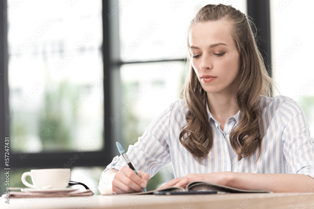 portrait of focused businesswoman writing in journal working in cafe portrait of focused businesswoman writing in journal working in cafe