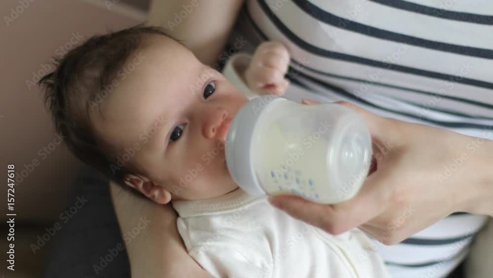 Baby is sucking milk from a bottle in his mother's arms (close-up) Baby is sucking milk from a bottle in his mother's arms (close-up)