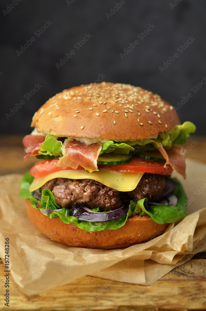 Beef burger with lettuce and bacon on wooden table Beef burger with lettuce and bacon on wooden table