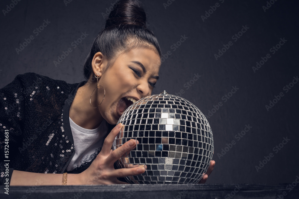 Naklejka premium glamour asian girl biting disco ball isolated on grey