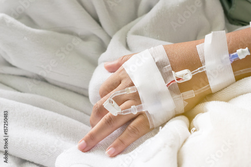 the Asian woman patient hand on IV drip with saline solution, fluid replacement therapy