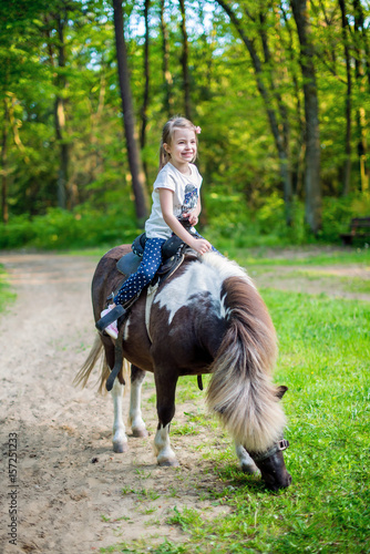 Happy smiling little girl on a pony in the forest