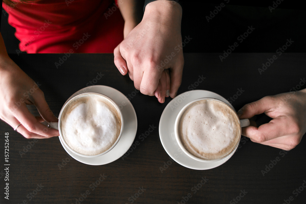 young couple sitting and drinking coffee at cafe restaurant. two cups with coffee are on table. hands of man and woman. people in love.