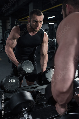 young sportsman holding dumbbells while looking at reflection in mirror