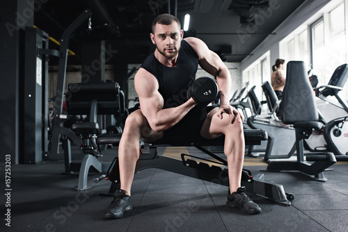 young sportsman doing biceps workout with dumbbell while looking at camera