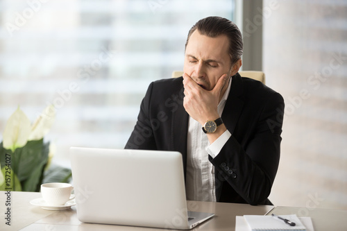 Photos Man yawning while sitting at desk in front of laptop