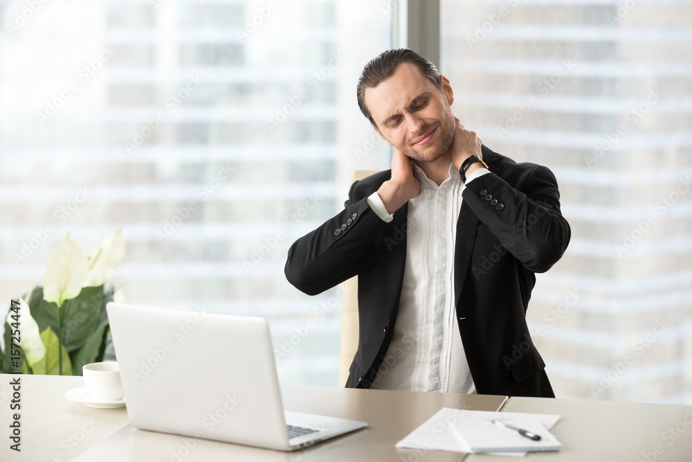 Businessman feeling pain in neck after sitting at desk. Tired man suffering of office syndrome after long hours work on computer. Entrepreneur massaging his tense neck muscles. Gymnastics at work Businessman feeling pain in neck after sitting at desk. Tired man suffering of office syndrome after long hours work on computer. Entrepreneur massaging his tense neck muscles. Gymnastics at work